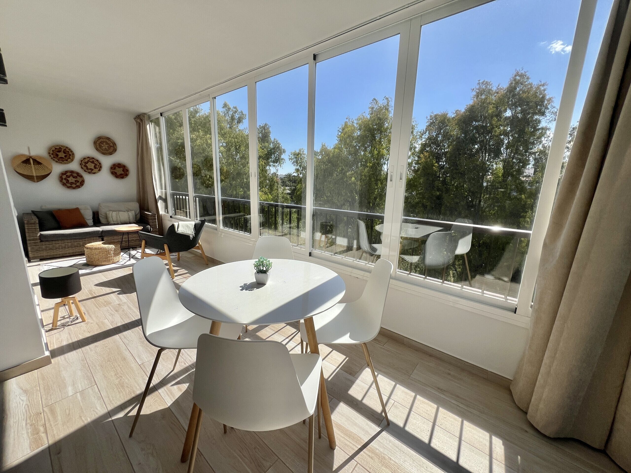 Una habitación luminosa con un ventanal grande, una mesa redonda con sillas, un sofá y placas decorativas en la pared.