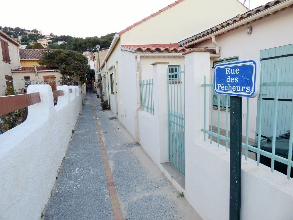 Una calle estrecha con un letrero que dice 'Rue des Pêcheurs' y un edificio de fachada blanca y contraventanas azules.