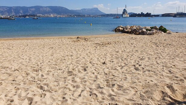 A sandy beach with boats in the water and a rocky outcrop in the foreground. - Beachfront, Comfortable, AIR CONDITIONER (ST MANDRIER SUR MER)