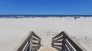 Une promenade en bois qui mène à une plage de sable, avec l’océan en arrière-plan.