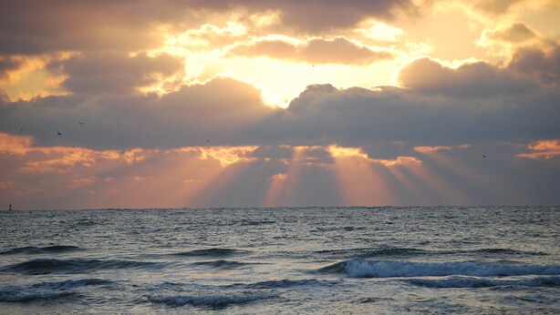 Un coucher de soleil sur l’océan, avec des vagues et des nuages.