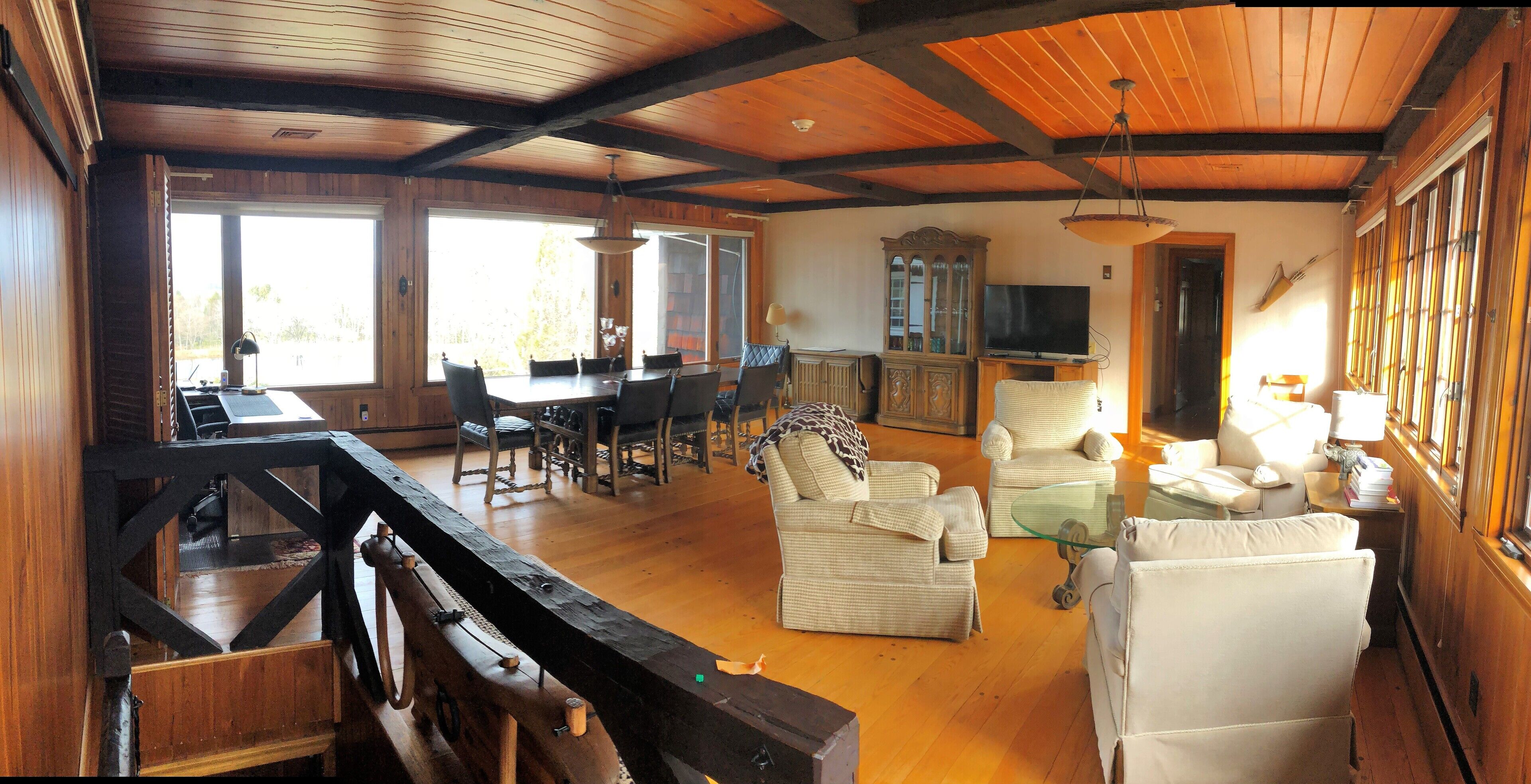 A spacious living room with a wooden ceiling, a dining area with a large table and chairs, and a cozy seating area with sofas and a television.