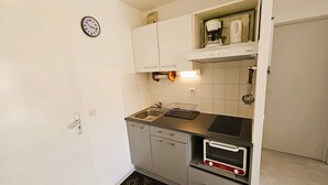 Pieni, käytännöllinen keittiö, jossa on pesuallas, mikroaaltouuni ja kahvinkeitin hyllyllä.