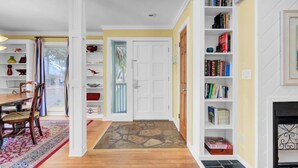 A hallway with a dining area, bookshelves, and a fireplace.