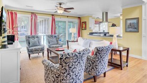 A living room with patterned armchairs, a white sofa, a dining table, and a ceiling fan.