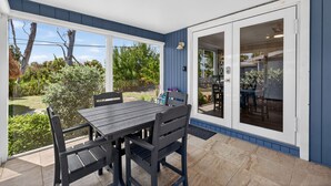 Une terrasse couverte avec une table et des chaises, une porte-fenêtre coulissante donnant sur un espace intérieur et une vue sur le jardin.