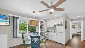Une cuisine moderne avec des meubles blancs, un coin repas doté d’une table ronde et de chaises, et un ventilateur de plafond.