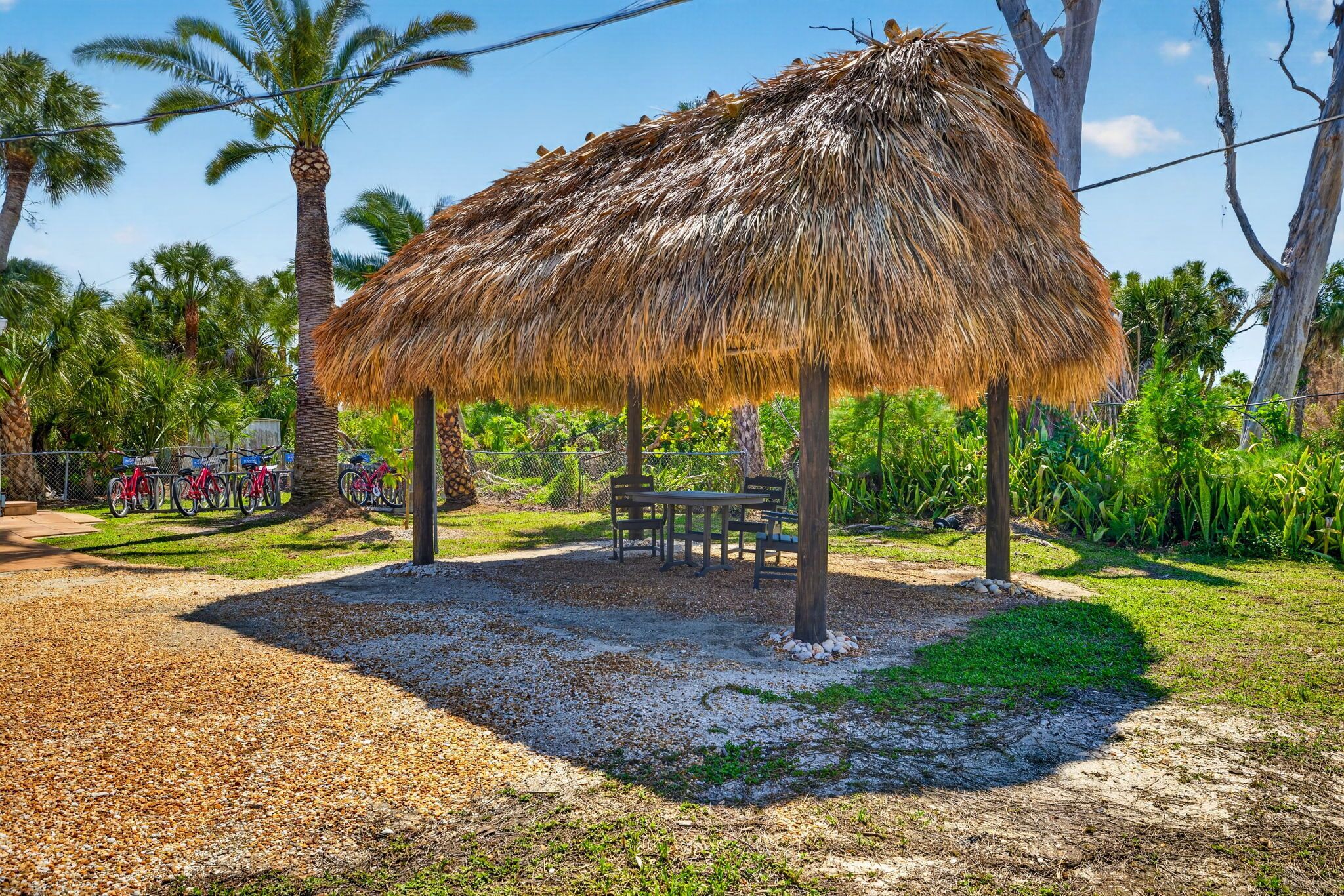 Una estructura con techo de paja, con una mesa y sillas, rodeada de palmeras y follaje.