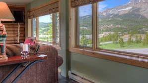 Una habitación acogedora con una mesa de madera, un sofá cómodo y grandes ventanales con vistas a la montaña.