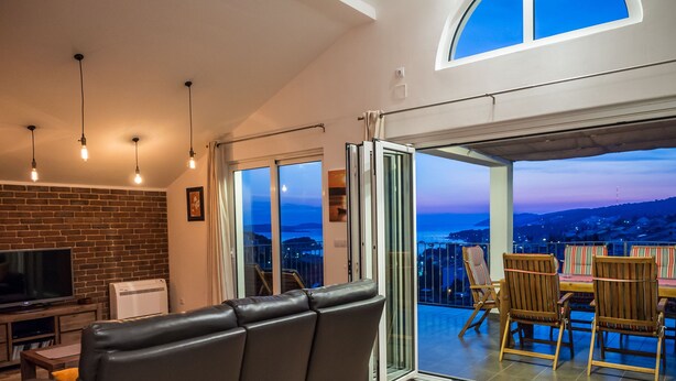 A modern living room with a leather sofa, a flat-screen TV, and a balcony with wooden chairs. - PENTHOUSE with SPECTACULAR SEA VIEW (Hvar)