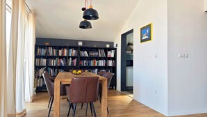 A dining area with a wooden table and chairs, a bookshelf filled with books, and a kitchen visible through an open doorway. - PENTHOUSE with SPECTACULAR SEA VIEW (Hvar)