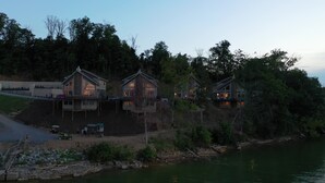 Three houses with balconies overlooking a body of water, surrounded by trees.