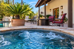 Un espace piscine comprenant un jacuzzi, des chaises longues et une table à manger.