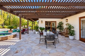 Un patio techado con suelo de piedra, mobiliario exterior y una piscina.