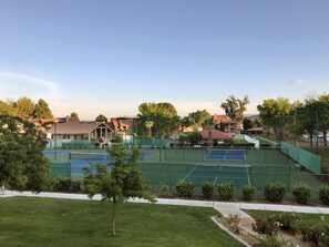 Una cancha de tenis con una cerca verde, rodeada de árboles y edificios.
