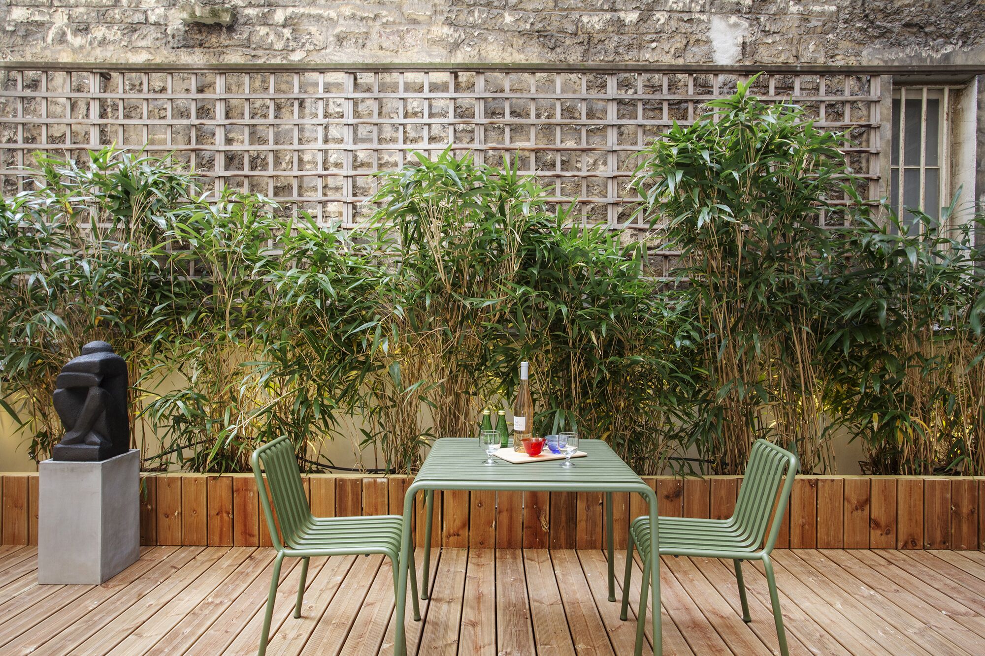 Un espacio de estar al aire libre con una mesa y sillas, rodeado de plantas de bambú y un muro de piedra.