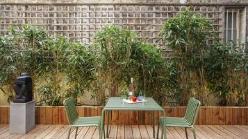 Un espacio de estar al aire libre con una mesa y sillas, rodeado de plantas de bambú y un muro de piedra.