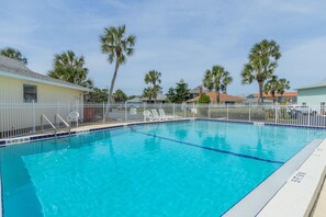 Une piscine d’un bleu éclatant, entourée d’une clôture blanche, de palmiers et de maisons.