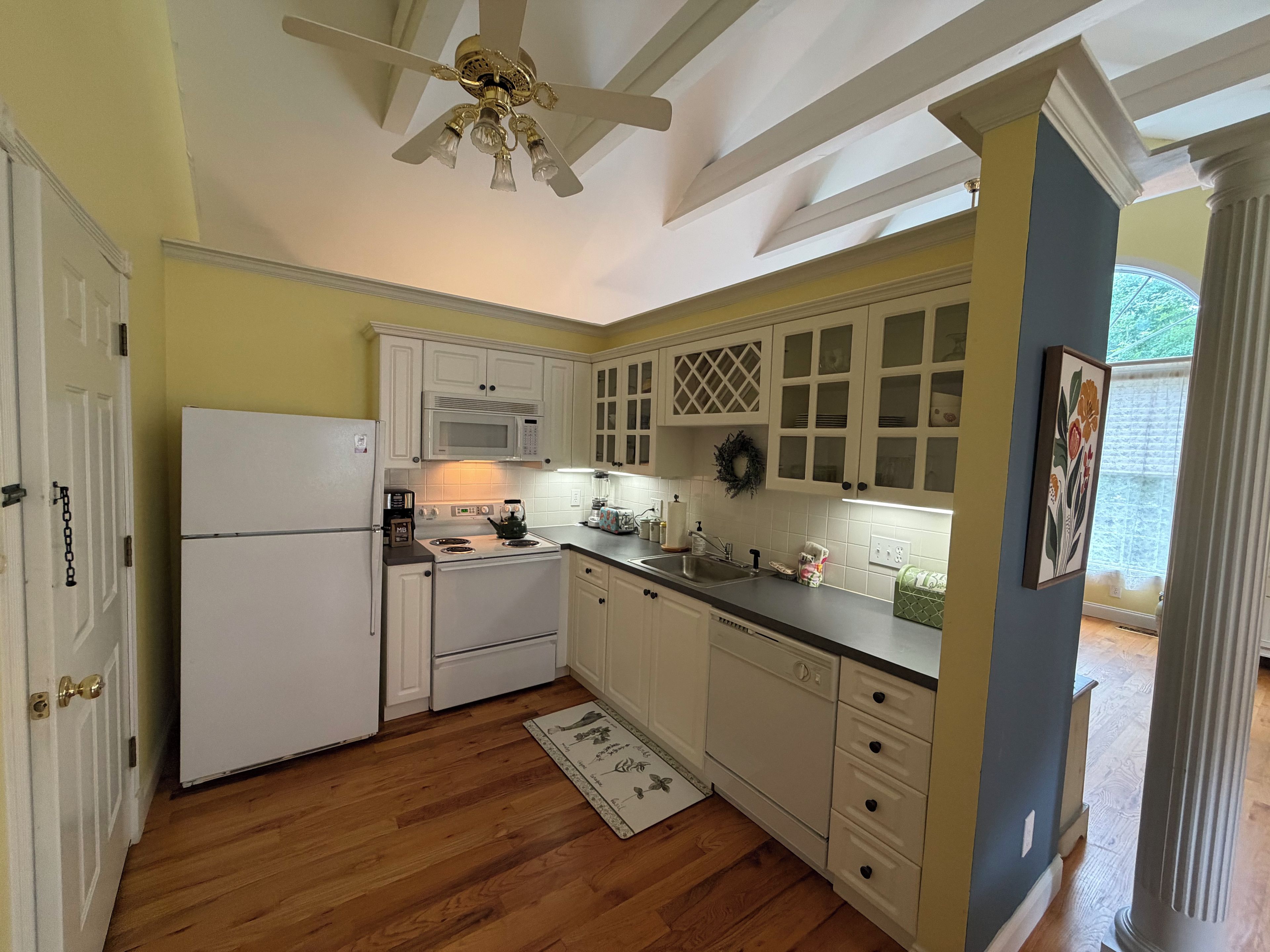 Una cocina con armarios blancos, un microondas, una estufa y un ventilador de techo.