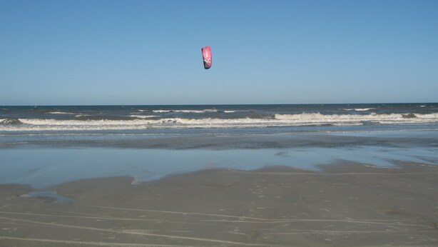 Une plage où l’on voit un pratiquant de kitesurf en plein vol.