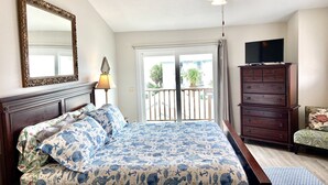 Une chambre à coucher comprenant un lit, une commode, un téléviseur et un balcon avec vue sur l’extérieur.