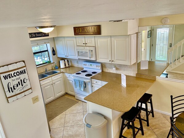 A kitchen with white cabinets, a stove, a microwave, and a sign that says 'WELCOME to our home.' - Best location in all of Jax Beach. Walk or bike ride to everything. (Jacksonville Beach)
