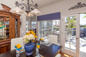 A dining area with a table set for four, a vase with flowers, and a view through the glass door to the outside.