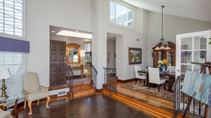 A spacious living area with a wooden staircase, a dining table with chairs, and a large window providing natural light. - Laguna Beach Tranquility Base across from Jr. High.  Long Term Discounts (Laguna Beach)