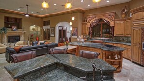 A spacious living area with a large L-shaped dining table, a fireplace, and a kitchen with wooden cabinetry and granite countertops.