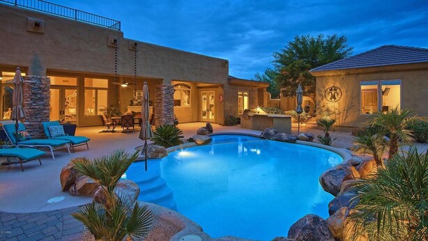 A pool area with lounge chairs and a stone pillar.