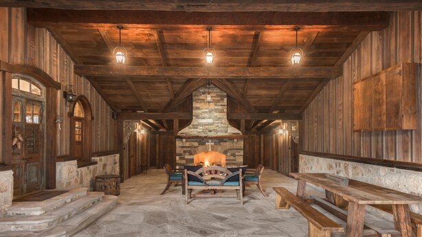 Ein rustikales Interieur mit Steinsäulen, Holzbänken und einem zentralen Kamin.