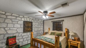Ein Schlafzimmer mit Steinwand, einem hölzernen Bett, einem Stuhl, einer Bank und einem Deckenventilator.