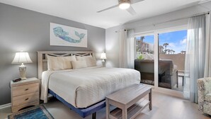 Un dormitorio con cama, lámparas de noche, ventilador de techo, ventana con vistas y una mesita.