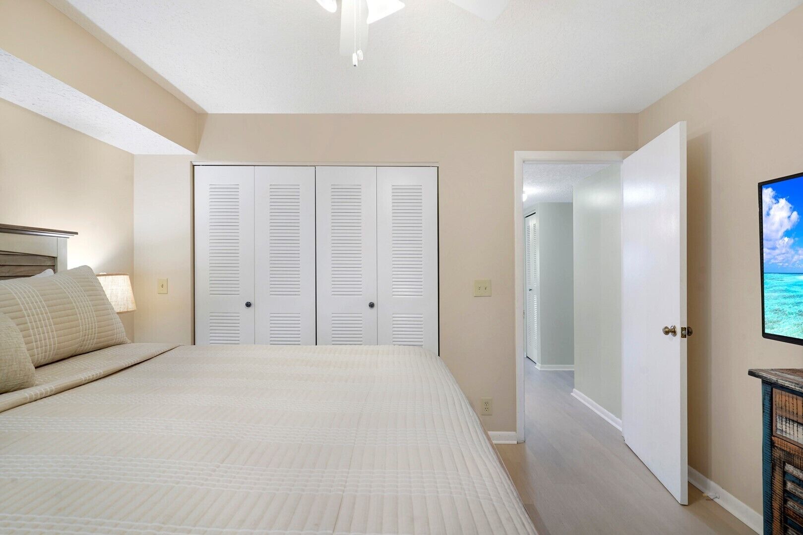 A bedroom with a bed, a closet, a door leading to another room, and a television on the wall.