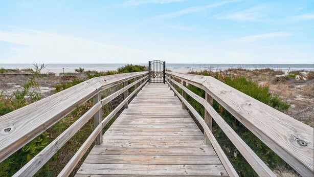 Un muelle de madera que lleva a un portón, rodeado de vegetación costera.
