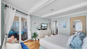 A bedroom with a large bed, a TV, a dresser, and a sliding glass door leading to a balcony.