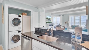 A modern kitchen with a built-in washer and dryer, a stainless steel sink, and a large window offering a view of the ocean.