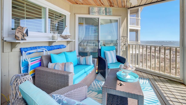 A covered outdoor seating area with wicker furniture, a ceiling fan, and a view of the beach.