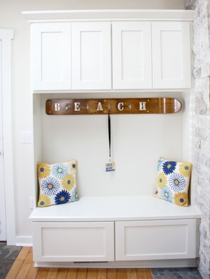 A white bench with floral cushions, a wooden sign spelling "BEACH", and a small name tag hanging from the sign.