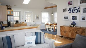 Eine moderne Küche mit Kochinsel, ein Essbereich mit Stühlen sowie ein Wohnzimmer mit Sofa und grauem Sessel.