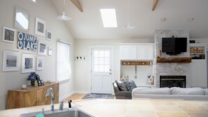 Amplia sala de estar con chimenea, televisor montado en una pared de piedra y cocina con lavabo y armarios.