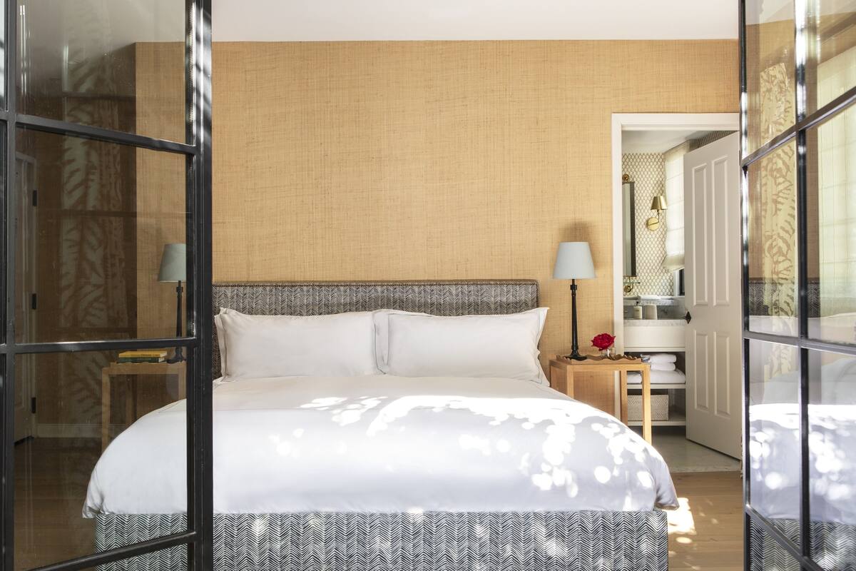 A hotel room with a bed, a nightstand, a lamp, and a view of the bathroom through an open door.