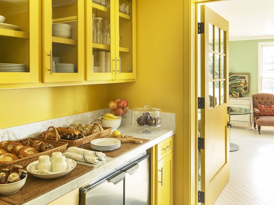 A kitchen with yellow cabinets, a stainless steel dishwasher, and a breakfast bar with various food items.