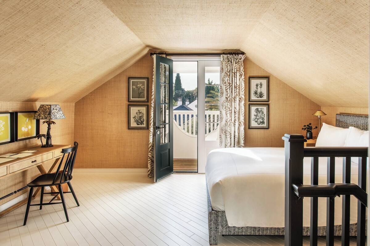 A bedroom with a bed, a desk, a chair, and a view of the outside.