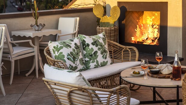 A cozy outdoor seating area with wicker furniture, a table with drinks, and a fireplace. - Hotel 850 SVB, a Member of Design Hotels (West Hollywood)