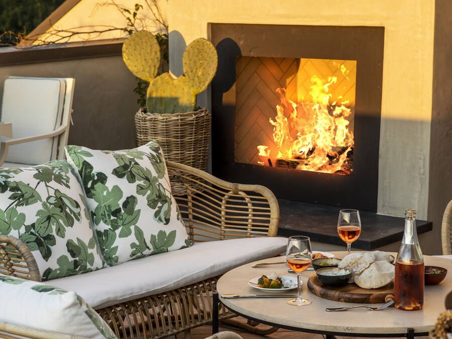 A cozy outdoor seating area with wicker furniture, a table with a bottle and glasses, and a fireplace.