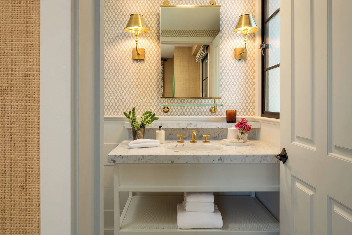 A bathroom with a marble sink, two wall-mounted lamps, a mirror, and a window.