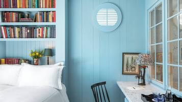 A bedroom with a bed, a bookshelf, a desk with a chair, a window, and a round wall decoration.