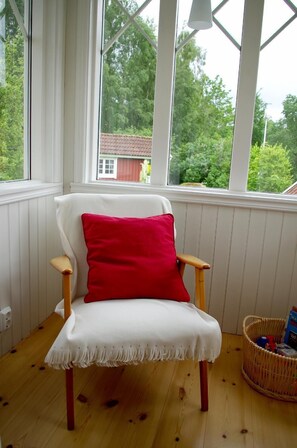 Una silla blanca con un cojín rojo en una habitación con piso de madera y paredes blancas.