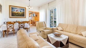 A spacious living room with a beige sofa, a dining area with a table and chairs, and a large window with curtains. - Ranias luxurious Apartment with sea view! (Chania)